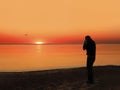 Back view of a silhouette of a man photographing the sun at sunset on the beach on holidays Royalty Free Stock Photo
