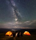 Back view travel team sitting near fire beside camping in night under wonderfull sky with many stars