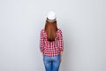 Back view snap model shot of young brunette woman in casual outfit and hat, standing on pure light grey background