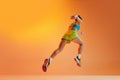 Back view. Sportive muscled woman, professional runner running away isolated on orange background in noen light. Sport