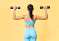 Back view of sporty woman in sportswear doing exercise with dumbbells on yellow background Royalty Free Stock Photo