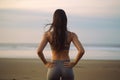 Back view of sporty young woman in sportswear standing on beach and looking away, Back view of woman athlete in sportswear doing