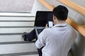 Back view of stressed young Asian business man sitting and using mobile smart phone and laptop at staircase of office. Royalty Free Stock Photo