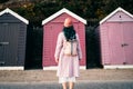 Back view stylish hipster woman with color hair in total pink outfit and backpack looking at wooden beach huts. Off