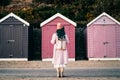 Back view stylish hipster woman with color hair in total pink outfit and backpack looking at wooden beach huts. Off