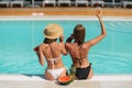 Back view of stylish women in swimsuits sitting and chilling with fruits near the pool. Tropical vacation. Summer mood. Royalty Free Stock Photo