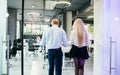 Stylish young man and woman at official style clothes which walking through the office room. Royalty Free Stock Photo