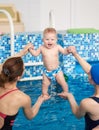 Back view of swimming trainer and mother lifting up little boy above blue pool water, teaching baby standing on his feet Royalty Free Stock Photo