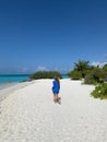 A back view of a tanned long-haired girl in a short blue dress running along the shores of the Indian Ocean with white sand and