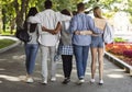 Back view of teen friends embracing and walking by park Royalty Free Stock Photo