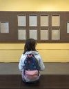 Back view of teen school girl with backpack sitting on bench in museum Royalty Free Stock Photo