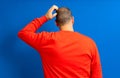 Back view of thoughtful man scratching his head over blue background. He wonders why he doesn& x27;t have luck in life Royalty Free Stock Photo