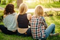 Back view of three beautiful women sitting on grass and hugs