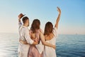 Back view of three best friends travelling by boat hugging and waving while looking at sea. People who are on luxury Royalty Free Stock Photo