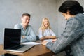 Back view of three cheerful young colleagues conducting business presentation while sitting at table with laptop and Royalty Free Stock Photo