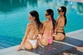 Three seductive girl sitting near swimming pool, sunbathing. Royalty Free Stock Photo