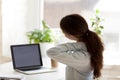 Back view of tired woman touching neck at work desk