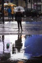 Back view to elegant young woman with transparent umbrella standing in rain weather reflecting