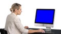 Young woman working in office, sitting at desk, looking at monitor, white background. Blue Screen Mock-up Display. Royalty Free Stock Photo