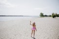 Back view to young blonde girl look like a Barbie doll in pink tones waving her hand on beach Royalty Free Stock Photo