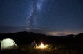 Tourist is relaxing near bonfire enjoying the silhouettes of mountains under starry sky with bright milky way Royalty Free Stock Photo