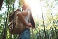 Back view on traveler backpack and hipster girl wearing hat. Young brave woman traveling alone among trees in forest on outdoors