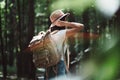 Back view on traveler backpack and hipster girl wearing hat. Young brave woman traveling alone among trees in forest on outdoors