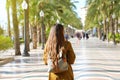 Back view of traveler girl walking on Explanada de Espana promenade of Alicante in the morning. Young female backpacker visiting