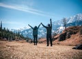 Back view of travelers with raised hands facing a scenic mountainscape, Kothi Meadows, Manali, India