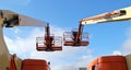 Back view of two aerial work platforms against blue sky with clouds.