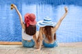 Back view of  two beautiful Young Asian women in big summer hat and sunglasses sitting on the edge of the swimming pool with feet Royalty Free Stock Photo