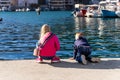 Back view two cute little curious sibling kids sitting on concrete embankment pier near sea lake bank and watching fish Royalty Free Stock Photo