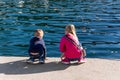 Back view two cute little curious sibling kids sitting on concrete embankment pier near sea lake bank and watching fish Royalty Free Stock Photo