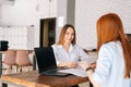 Back view of two positive young business women discussing new project sharing ideas sitting at desk opposite each other Royalty Free Stock Photo