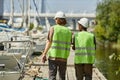 Back view two workers wearing hardhats walking on pier in yacht docks