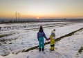 Back view of two young children in warm clothing standing in frozen snow field holding hands on copy space background of setting Royalty Free Stock Photo