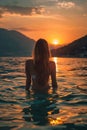 Back View of Unrecognizable Female Silhouette Standing in Rippling Sea Water Enjoying Sunset Over Mountains Royalty Free Stock Photo