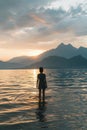 Back View of Unrecognizable Female Silhouette Standing in Rippling Sea Water Enjoying Sunset Over Mountains Royalty Free Stock Photo