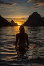 Back View of Unrecognizable Female Silhouette Standing in Rippling Sea Water Enjoying Sunset Over Mountains Royalty Free Stock Photo