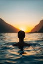 Back View of Unrecognizable Female Silhouette Standing in Rippling Sea Water Enjoying Sunset Over Mountains Royalty Free Stock Photo