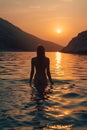 Back View of Unrecognizable Female Silhouette Standing in Rippling Sea Water Enjoying Sunset Over Mountains Royalty Free Stock Photo