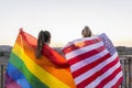 Back view unrecognizable lesbians couple holding lgtb rainbow flag and American flag at sunset.United States and gay pride flags