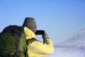 Back view of unrecognizable male in hat and backpack taking picture of amazing winter landscape