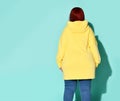 Back view of a voluptuous lady in jeans and bright yellow hoodie putting capuche on her head.