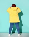 Back view of a voluptuous lady in jeans and bright yellow hoodie putting capuche on her head.