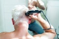 Back view white hair man doing self haircut with a clipper and looks in the mirror. Self-care at home in the conditions Royalty Free Stock Photo