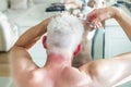 Back view white hair man doing self haircut with scissors and looks in the mirror. Self-care at home in the conditions Royalty Free Stock Photo