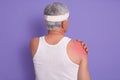 Back view of white haired senior man posing in studio against lilac wall, male being injured in gym, doing physical exercises,