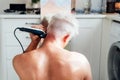 Back view white, silver hair man doing self haircut with a clipper and looks in the mirror. male self-care at home with electric Royalty Free Stock Photo