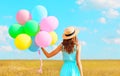 Back view woman with an air colorful balloons in a straw hat enjoying a summer day on a field and blue sky Royalty Free Stock Photo